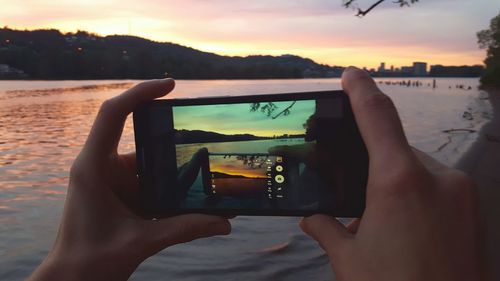 Midsection of man photographing sea against sky during sunset