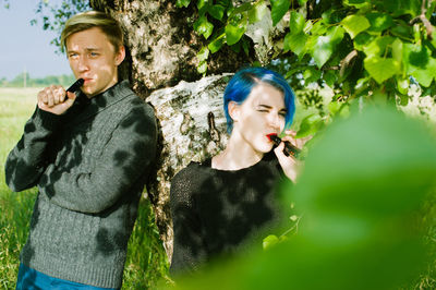 Friends smoking while standing by tree on field