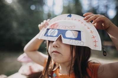 Girl holding solar eclipse glasses and mask while playing at park