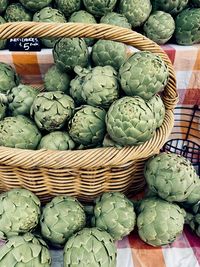 Basket filled with whole green artichokes in tabletop display at farmers market 
