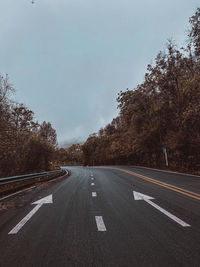 Empty road amidst trees against sky