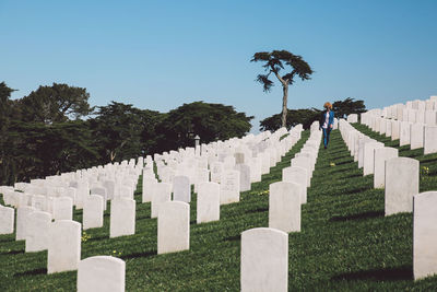 Mid adult woman walking at cemetery against clear blue sky