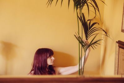 High angle view of mid adult woman looking at plant while sitting against wall