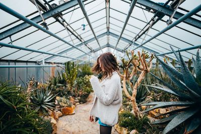 Rear view of woman standing in greenhouse