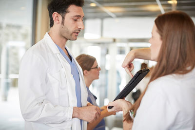 Young healthcare workers discussing over digital tablet while standing in lobby at hospital