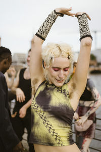 Carefree non-binary person showing armpit hair with friends in background