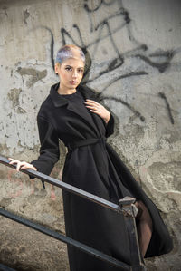 Portrait of young woman standing against wall