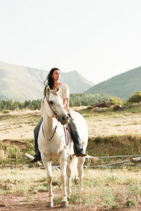 Woman horseback riding on grassy field against clear sky