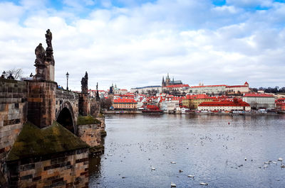 Charles bridge over vltava river against cloudy sky in city