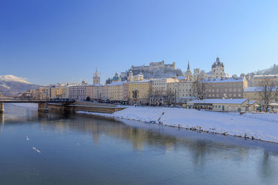 River in city against clear blue sky during winter