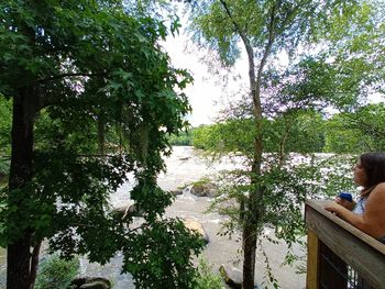 Rear view of man standing by lake against trees