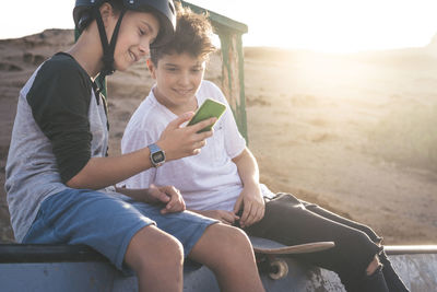 Boy showing smart phone to friend while sitting outdoors