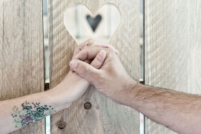 Cropped image of couple holding hands by wooden fence