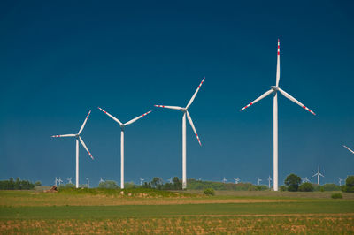 Wind turbines on field against clear blue sky