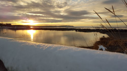 Frozen railing by sea against sky at sunset