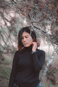 Young woman standing by tree against plants