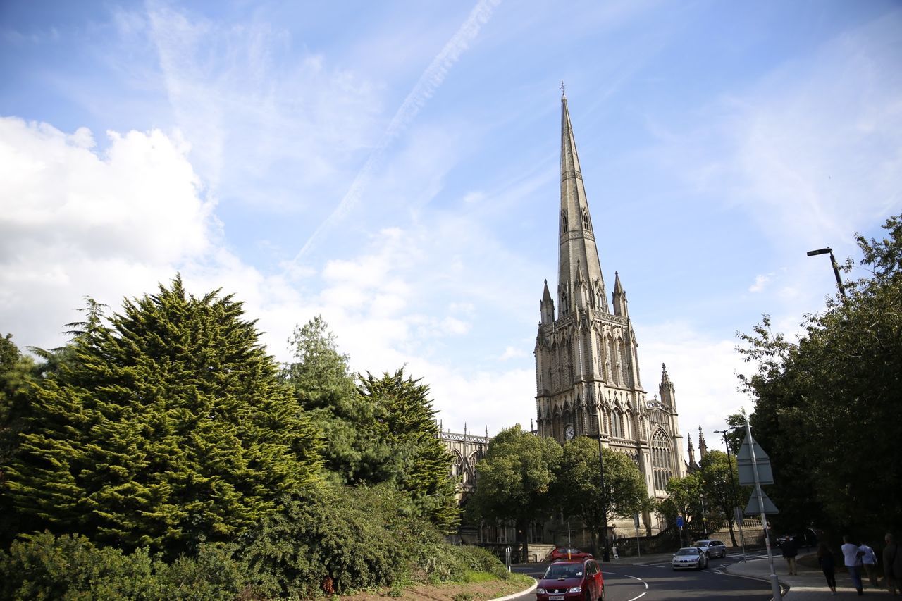 architecture, building exterior, built structure, tree, sky, religion, church, low angle view, transportation, tower, car, cloud - sky, place of worship, road, street, cloud, spirituality, city