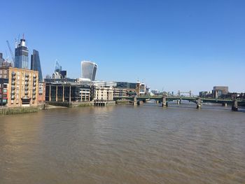 View of buildings by river against clear blue sky