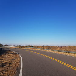 Road by land against clear blue sky