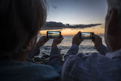 Rear view of couple photographing from mobile phones at beach