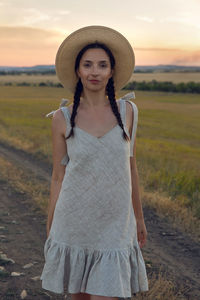 Woman in the hat and dress is on the field at sunset on the track