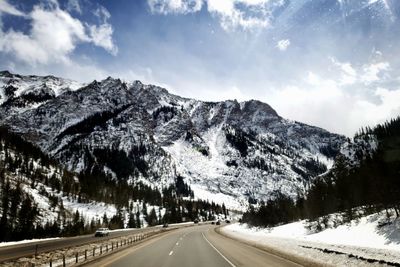 Road by snowcapped mountains against sky during winter