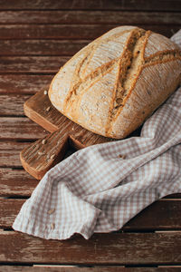 Freshly baked bread loaf on rustic wooden cutting board and napkin