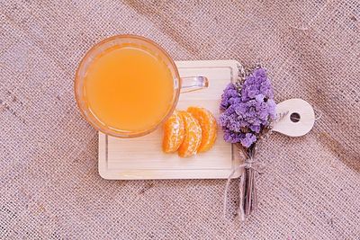 High angle view of orange juice with flowers on burlap