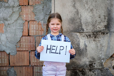 Portrait of cute girl holding poster against wall