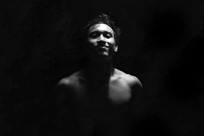 Portrait of shirtless man standing against black background