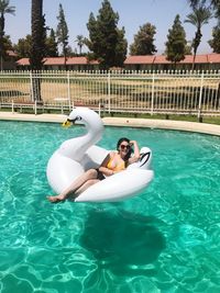 Young woman on inflatable swan in swimming pool