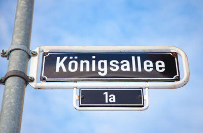 Low angle view of metallic koenigsallee road sign against sky