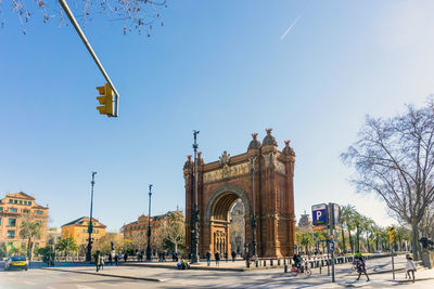 People walking by arc de triomf during sunny day