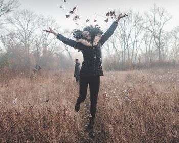 Full length of woman jumping while throwing dry leaves on field