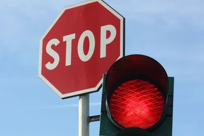 Low angle view of stop sign by illuminated red light against sky