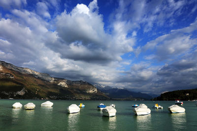 Boats sailing in lake by mountains against sky