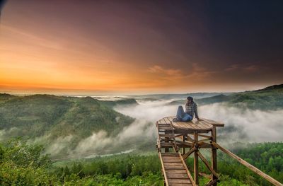 Man sitting on built structure against sky during sunset