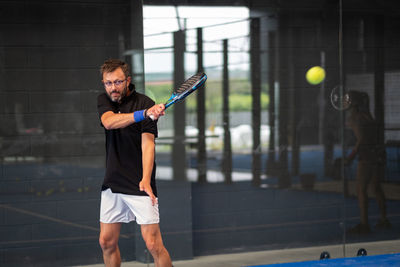 Man playing padel in a blue grass padel court indoor - young sporty boy padel player hitting ball 