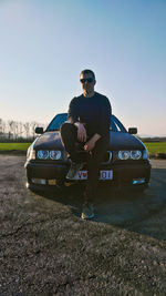 Side view of man on car against sky on field