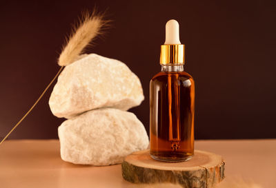 Transparent glass cosmetic dropper on wooden podium near stones and dry flowers on dark backdrop 