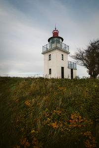 Lighthouse on field by building against sky