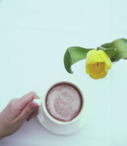 Cropped hand holding coffee by yellow tulip on table