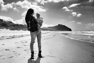 Mother carrying daughter at beach against sky
