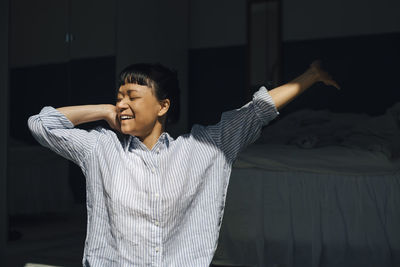 Smiling woman stretching in bedroom at home