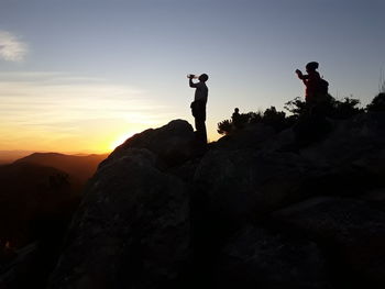 Silhouette man standing on rock against sky during sunset