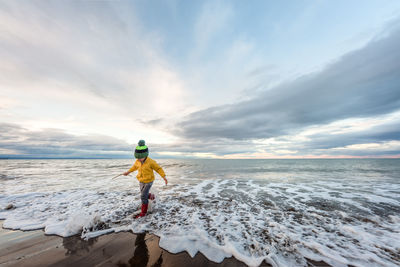 Preschooler running in water with boots and hat in new zealand