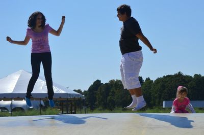 Siblings jumping on trampoline against sky in park