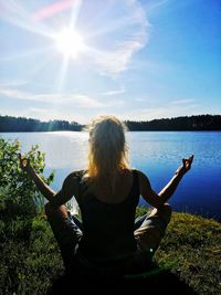 Rear view of woman sitting by lake against sky