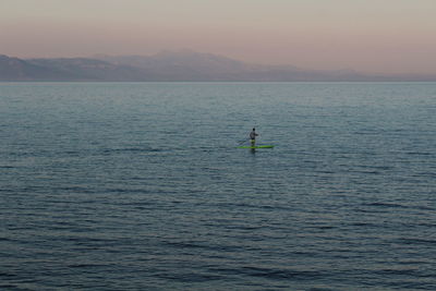 Man paddleboarding on river against sky during sunset