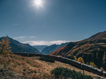 Train passing by mountains on sunny day